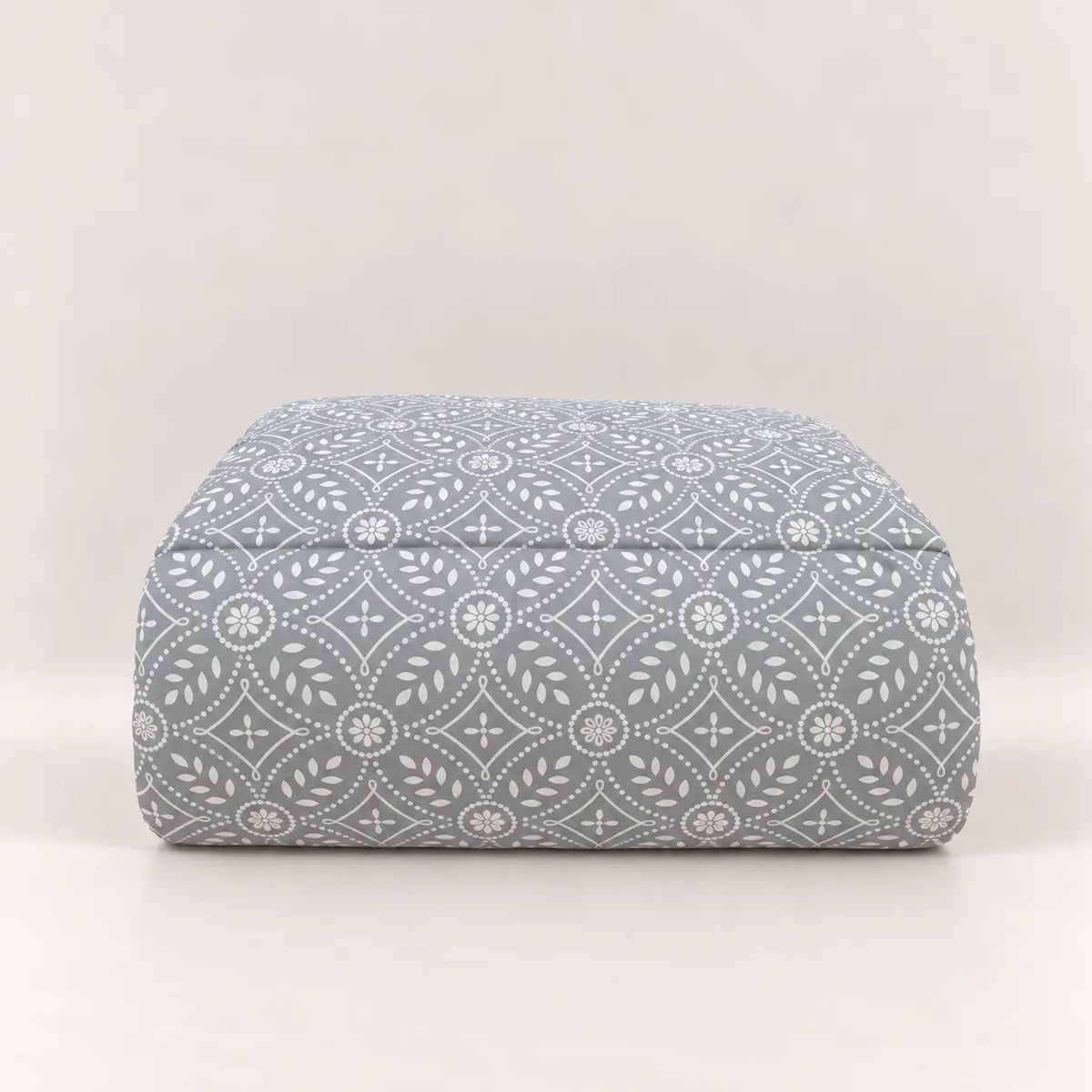 Edredón de invierno azul grisáceo con patrón geométrico blanco, perfectamente doblado bajo sus dos fundas de almohada lisas a juego.