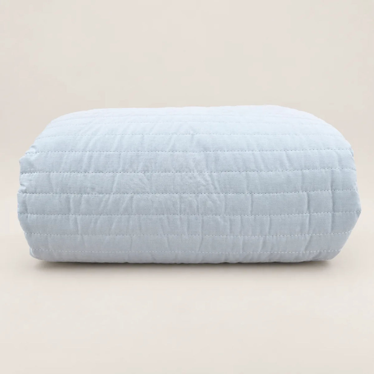 Cubrecama ligero de verano doblado, destacando su suave funda de algodón percal azul cielo, el pespunte de rayas y el volante decorativo.