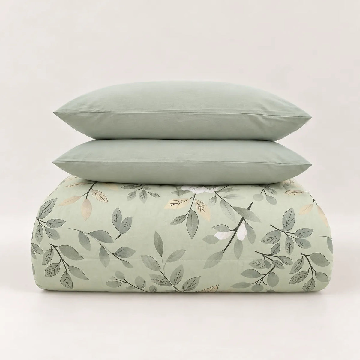Edredón de invierno verde claro con estampado botánico de hojas, doblado cuidadosamente bajo sus dos fundas de almohada lisas a juego.